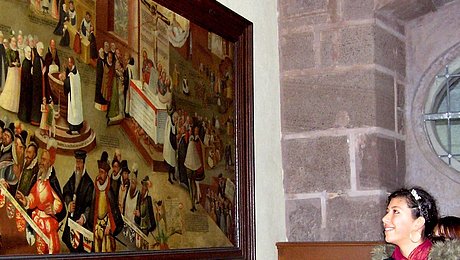 Fotoaufnahme der Führung „Bekenntnis – wozu wir uns bekennen“ in der Bad Windsheimer Spitalkirche. An einer Wand hängt ein Gemälde im Holzrahmen. Davor stehen zwei Jugendliche, die es betrachten. Die Wand rechts daneben besteht aus Sandsteinquadern. 